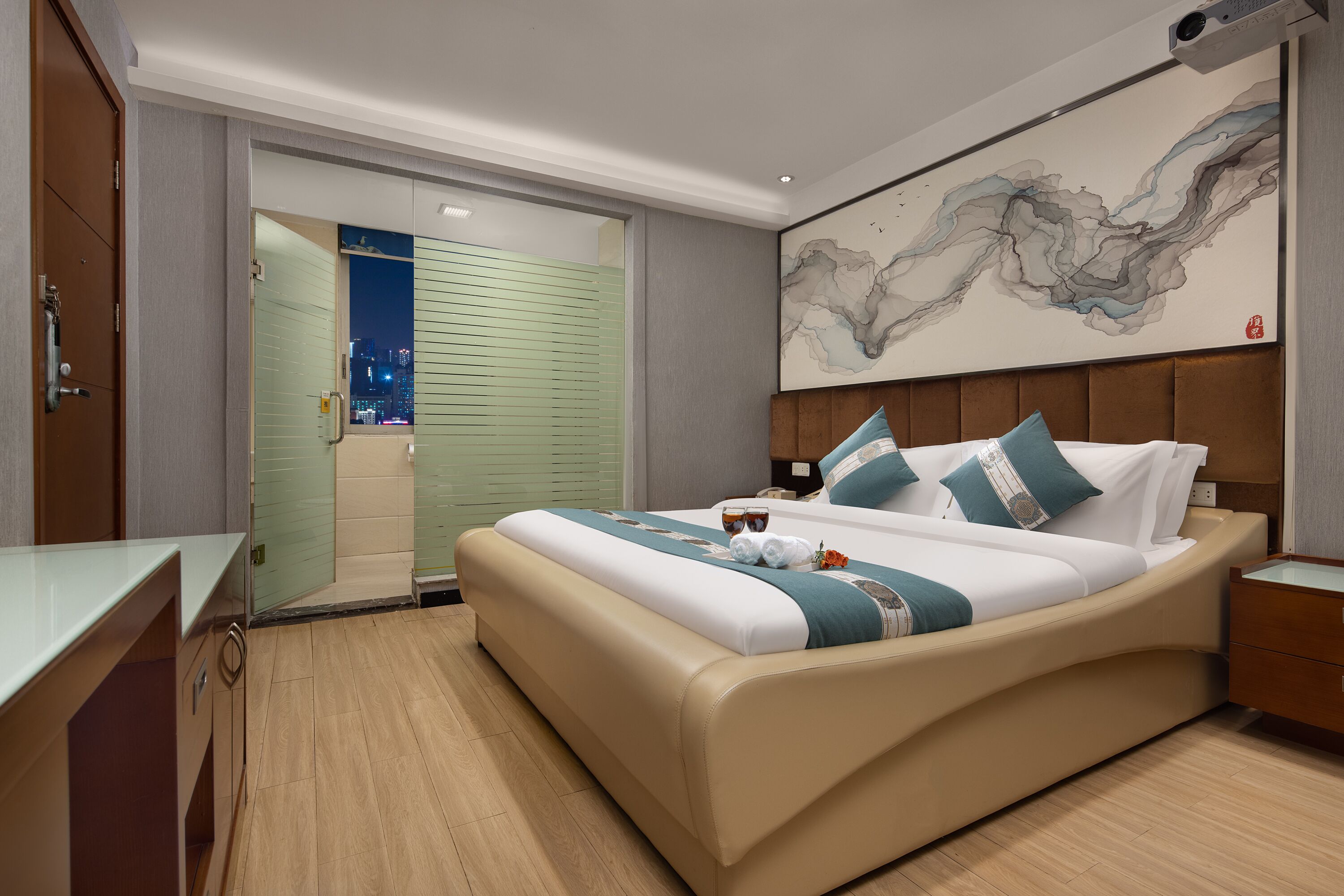 A modern hotel room with a large bed, a desk, and a view of the city at night.