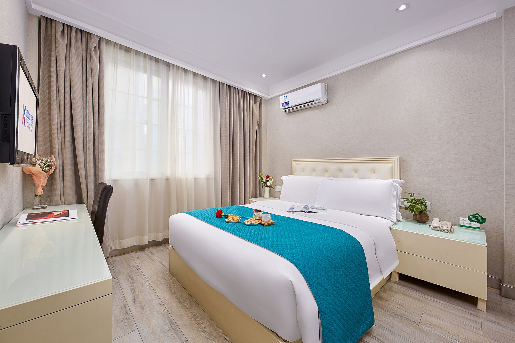A hotel room with a bed, bedside table, nightstand, and an air conditioning unit.