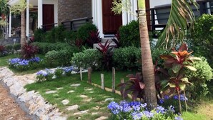 Un edificio moderno de varios pisos con balcón, rodeado de jardines cuidados y palmeras.