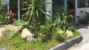 Una casa moderna con fachada de vidrio, un porche cubierto y un jardín cuidado con diversas plantas y una roca como elemento central.