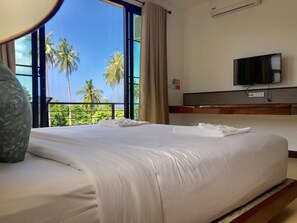 A hotel room with a large bed, a television, and a view of palm trees through the window. - Field-d House (Koh Tao)