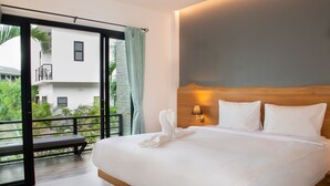 Habitación de hotel con una cama grande, cabecera de madera, mesita de noche con lámpara y balcón con banco.