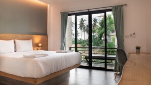 Habitación de hotel con una cama grande, un escritorio y vistas a palmeras a través de la ventana.