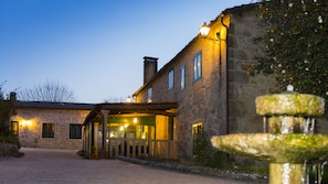 A stone building with a covered entrance and a fountain in the foreground.