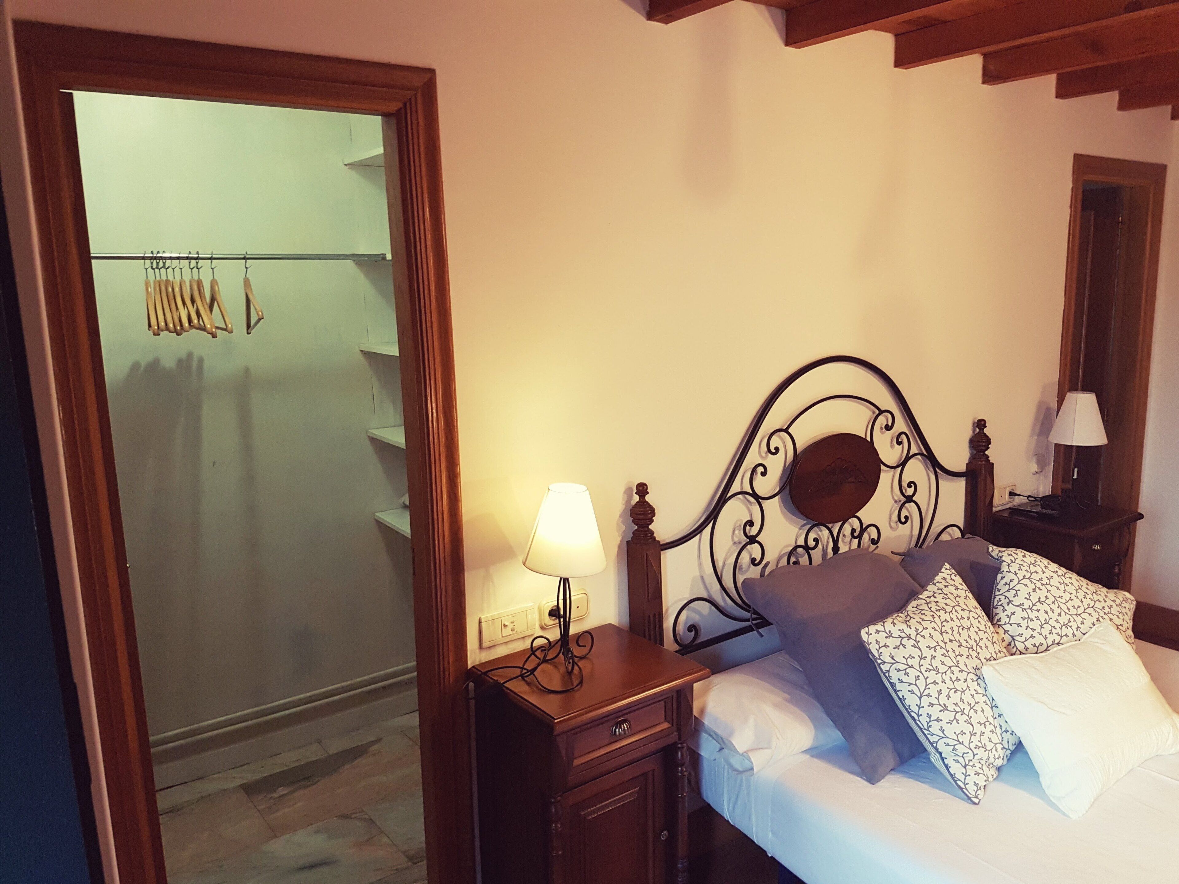 A bedroom with a bed, a nightstand, a lamp, a wooden headboard, and a wardrobe.