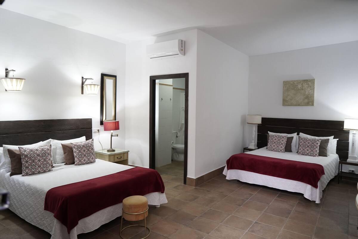 Habitación de hotel con dos camas, un baño y un taburete pequeño.