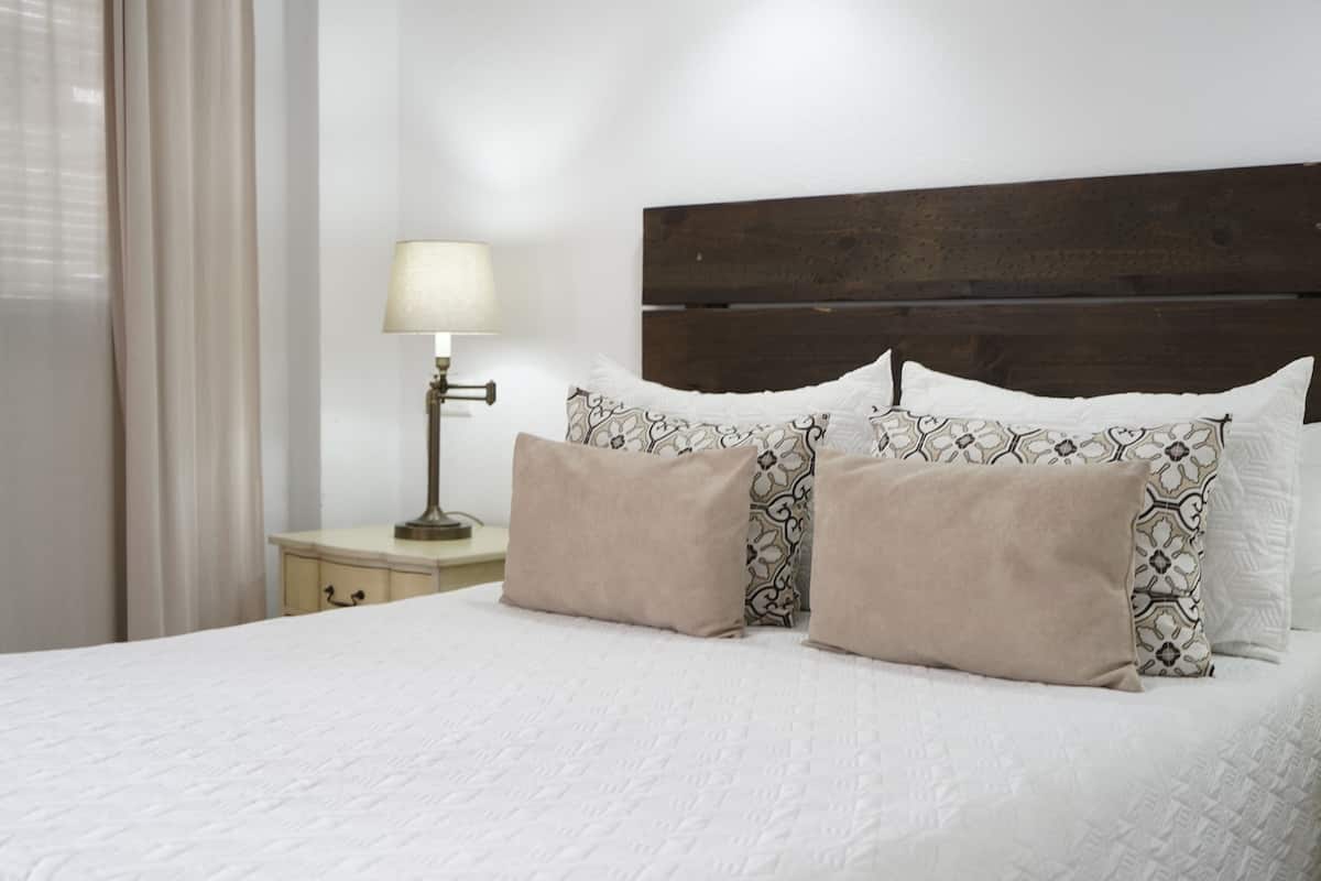 Una cama bien hecha con almohadas estampadas, una lámpara de noche y un cabecero de madera.