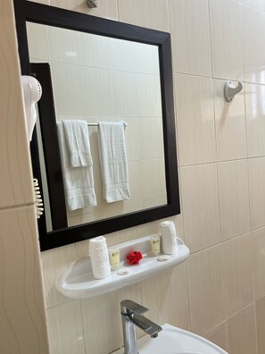 Ein Badezimmer mit einem großen Spiegel, weißen Fliesen, einem Waschbecken mit Pflegeprodukten und einem Handtuchhalter.