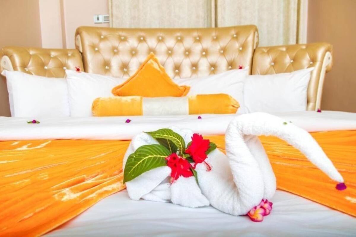 Une chambre d’hôtel avec une tête de lit capitonnée, du linge de lit blanc et une disposition décorative des serviettes.