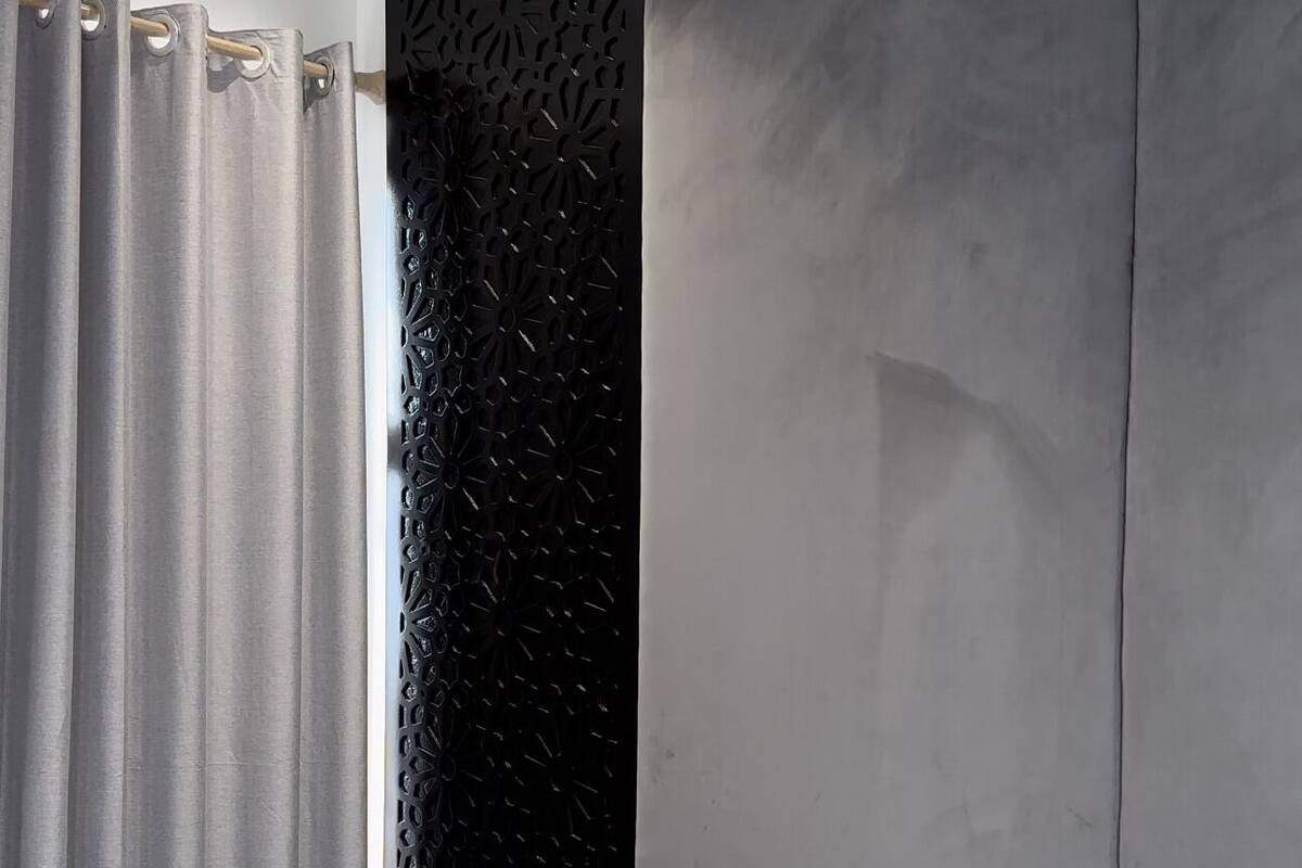 Une chambre moderne avec un grand lit, des rideaux gris, un panneau décoratif noir et une tête de lit grise.