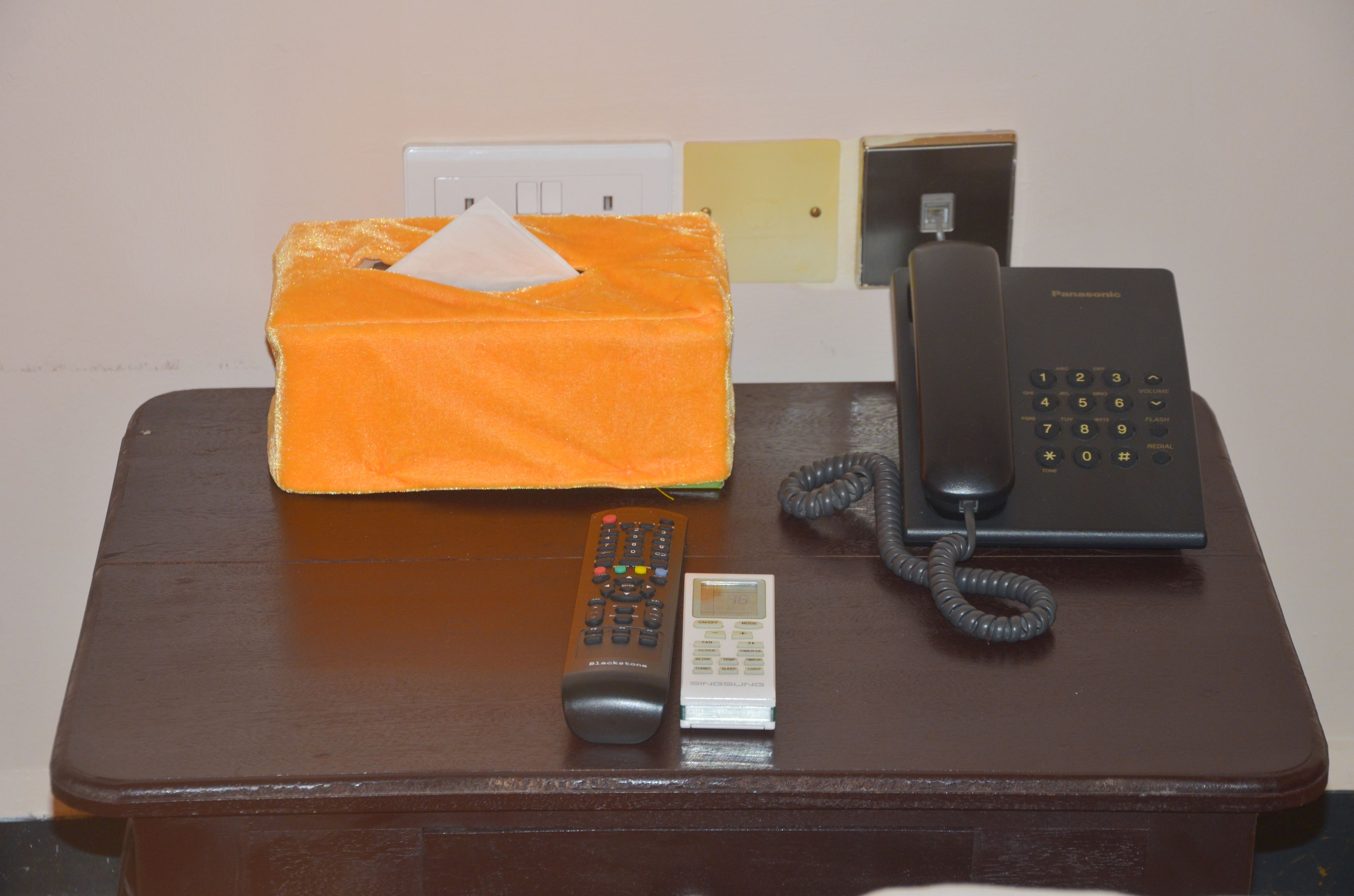 A wooden table with a black telephone, a remote control, and an orange tissue box.