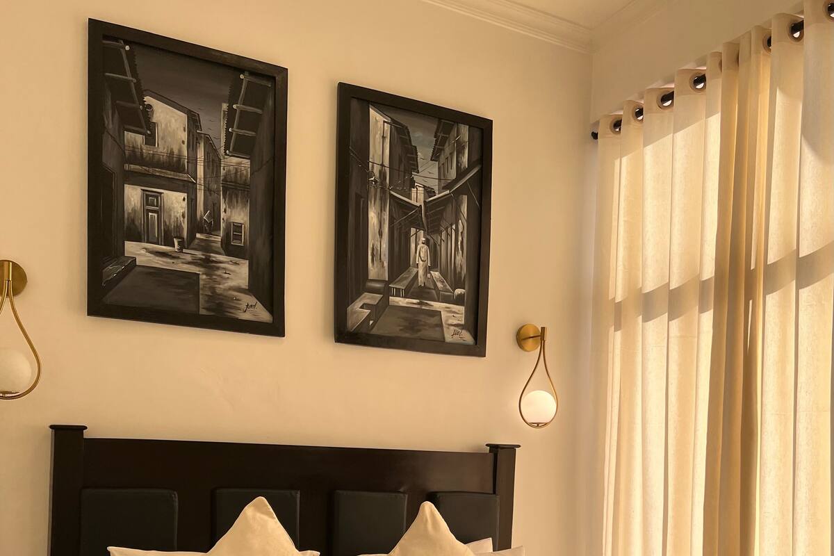 Un lit bien fait, avec une literie blanche et des oreillers, une tête de lit sombre et deux œuvres d’art encadrées accrochées au mur.