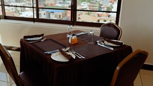Une table à manger dressée pour quatre personnes, avec vue sur la ville grâce à de grandes fenêtres.