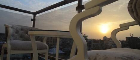 A balcony with a view of the sunset, featuring two chairs and a table.
