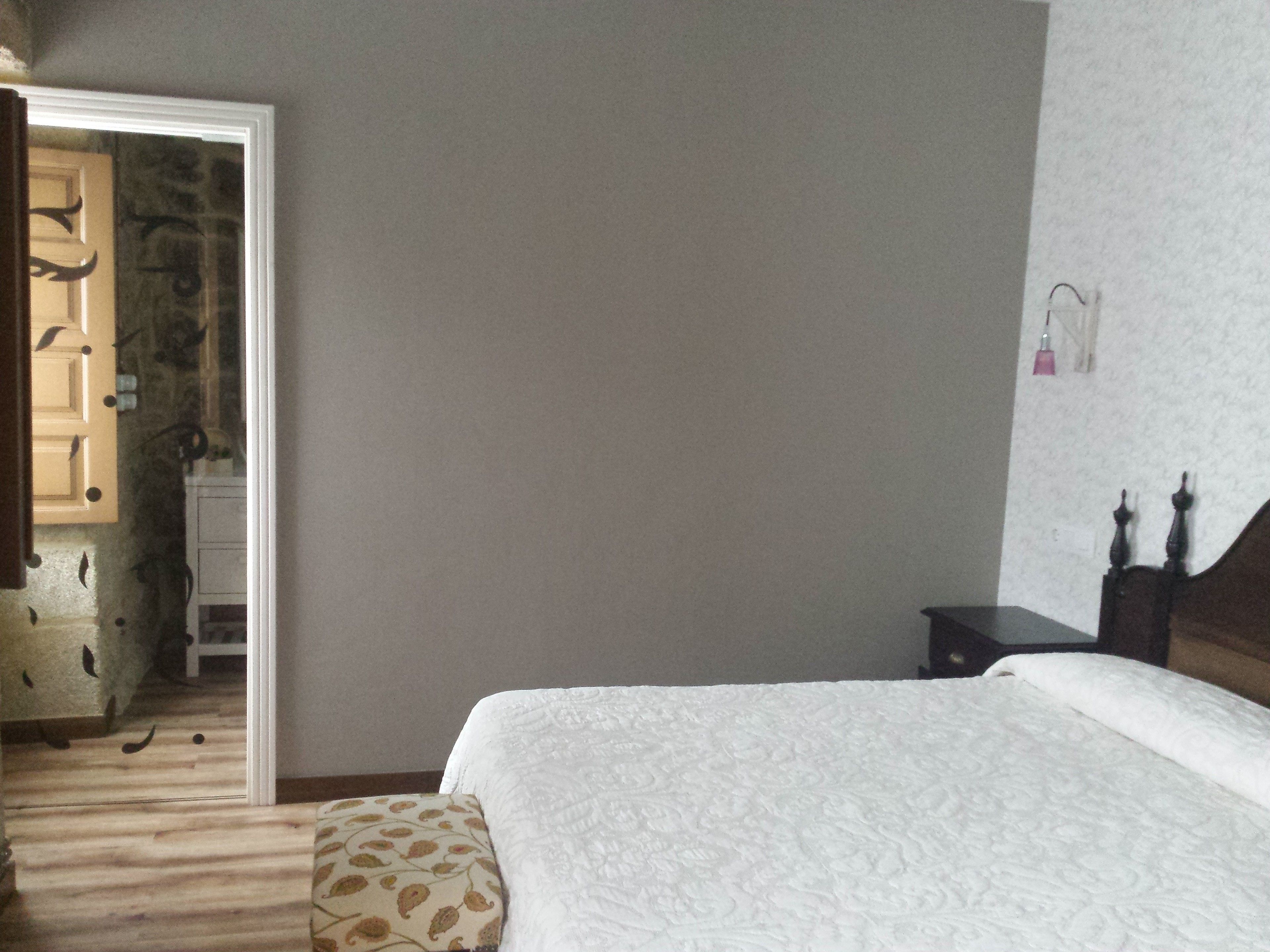 A bedroom with a bed, a wooden floor, a door, and a wall-mounted light fixture.
