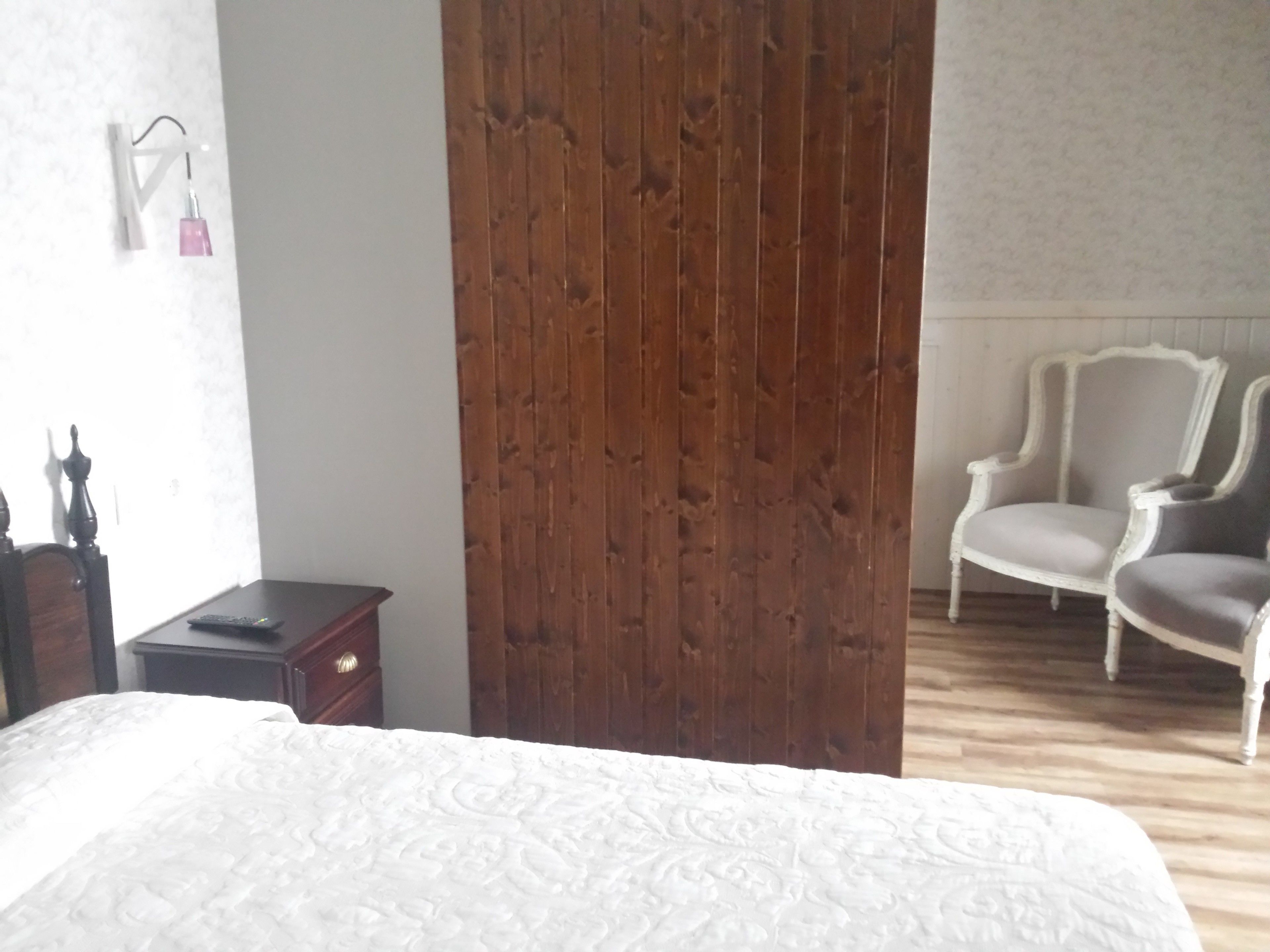 A bedroom with a wooden wardrobe, a bed with a patterned bedspread, a nightstand, a chair, and a dresser.