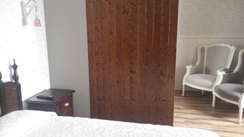 A bedroom with a wooden wardrobe, a bed with a patterned bedspread, a nightstand, a chair, and a dresser.