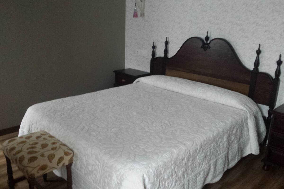 Une chambre à coucher avec un lit en bois, une table de chevet, une petite table et une chaise dotée d’un coussin à motifs.