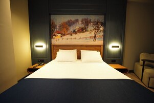 A hotel room with a large bed, two bedside tables, a painting on the wall, and a chair.