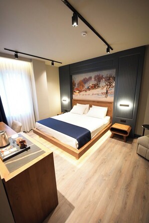 A modern hotel room with a large bed, a desk with a coffee maker, and a painting on the wall. - Jaleriz Hotel (Gaziantep)