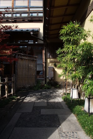 A narrow pathway leading to a traditional Japanese building with a tiled floor, bamboo plants, and a wooden fence. - Zen Oyado Nishitei (Fukuoka)