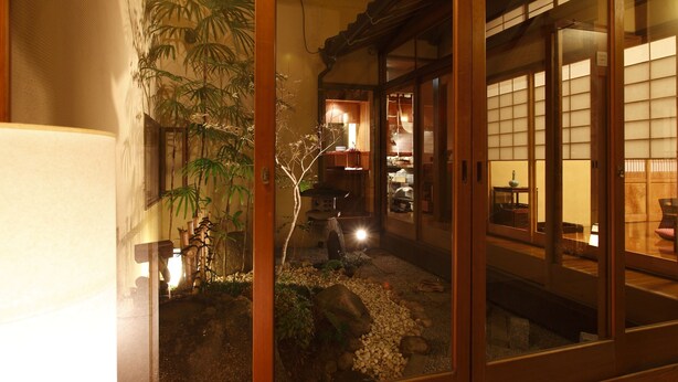 A traditional Japanese interior with sliding doors, a small garden area with rocks and plants, and a glimpse of a dining area in the background. - Zen Oyado Nishitei (Fukuoka)