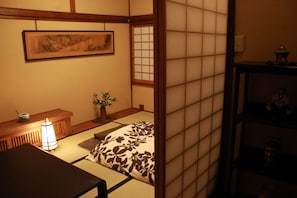 A traditional Japanese room with tatami flooring, a low wooden table, a cushioned bench, a hanging picture, and a sliding door. - Zen Oyado Nishitei (Fukuoka)