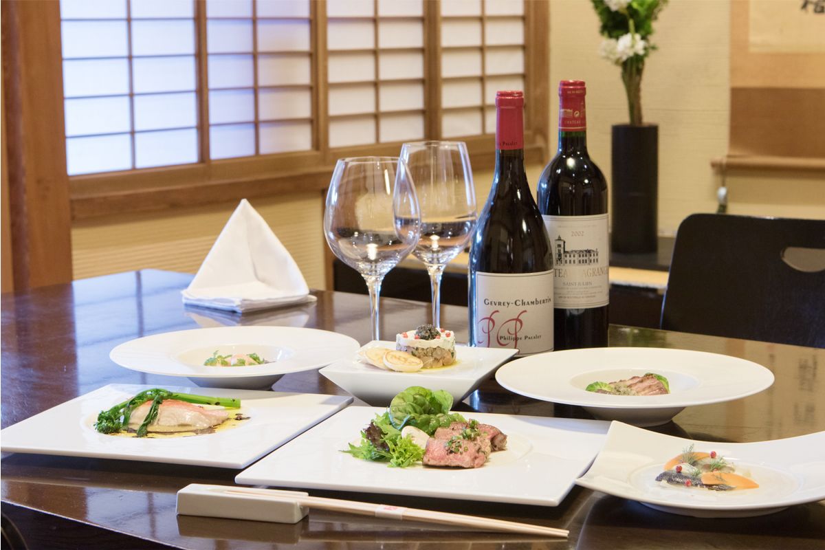 A dining table with plates of food, wine glasses, and bottles of wine.