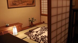 A traditional Japanese room with tatami flooring, a low wooden desk, a hanging painting, and a shoji screen door. - Zen Oyado Nishitei (Fukuoka)