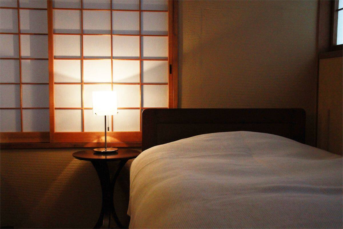 Une chambre d’hôtel avec un lit, une table de chevet avec une lampe et une vue sur une fenêtre de style japonais traditionnel.