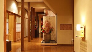 A hallway with wooden flooring, a large vase with flowers, and a staircase in the background. - Zen Oyado Nishitei (Fukuoka)