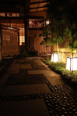 Un jardín japonés tradicional con senderos de piedra, plantas de bambú y faroles iluminados.