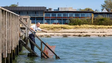 Una persona en un muelle de madera que se adentra en una masa de agua, con un edificio al fondo.