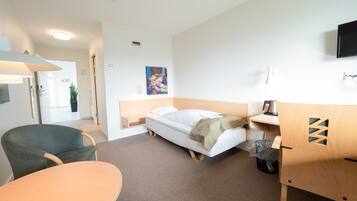 A hotel room with a bed, a desk, a chair, a TV, and a painting on the wall.