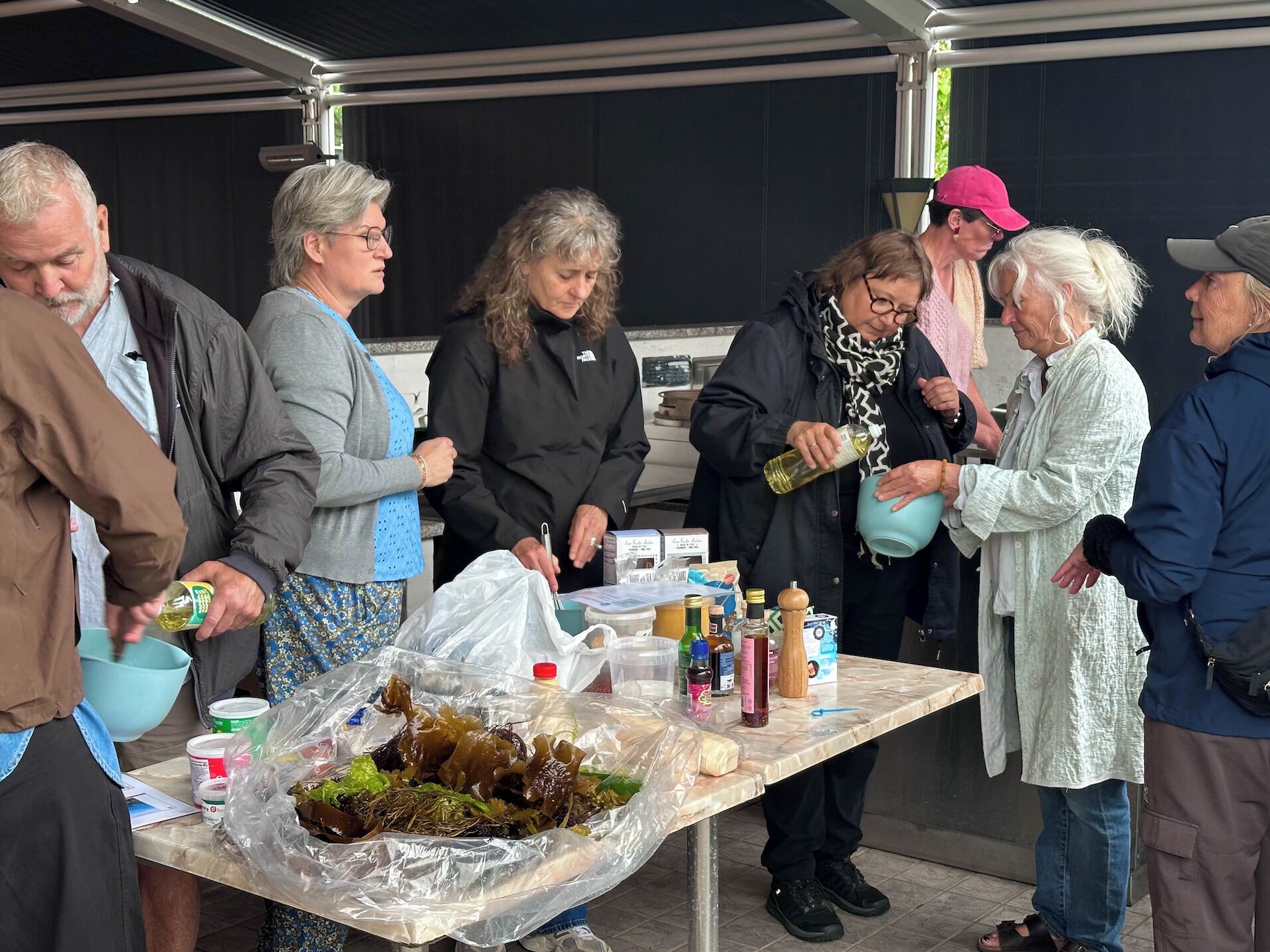 A group of people gathered around a table with food items and condiments.