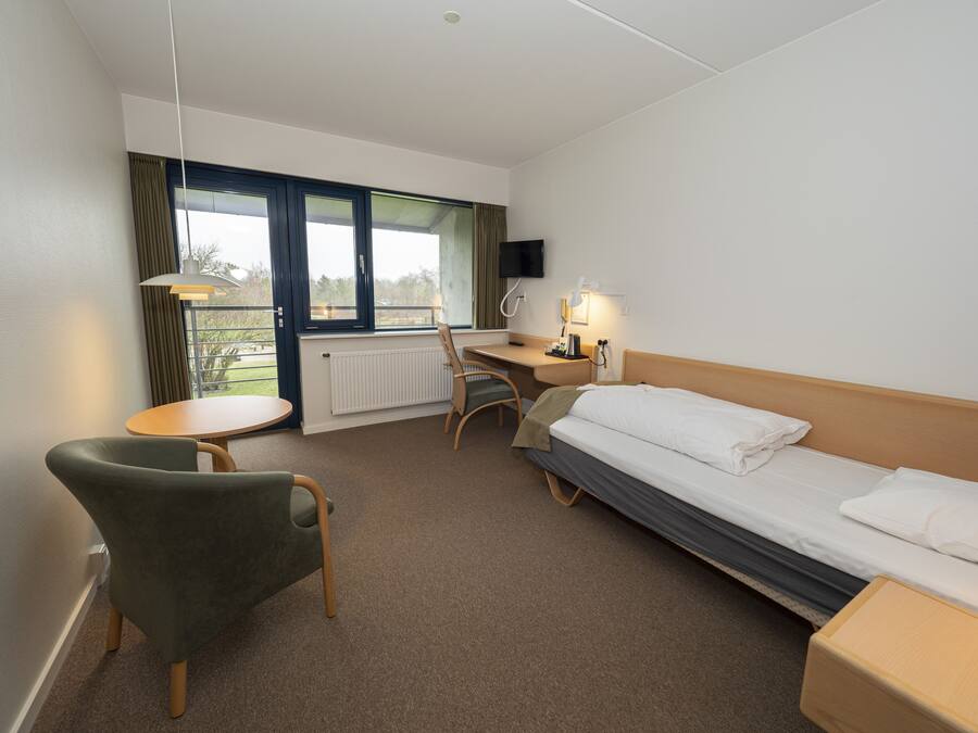 Quarto de hotel com cama, escrivaninha, cadeira, mesa e televisão.