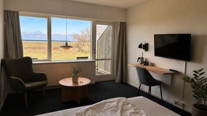 Habitación de hotel con una cama, un escritorio con computadora, una silla, un televisor y una ventana con vistas al exterior.