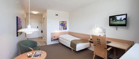 A hotel room with a bed, a desk, a chair, a table, a TV, and artwork on the walls.