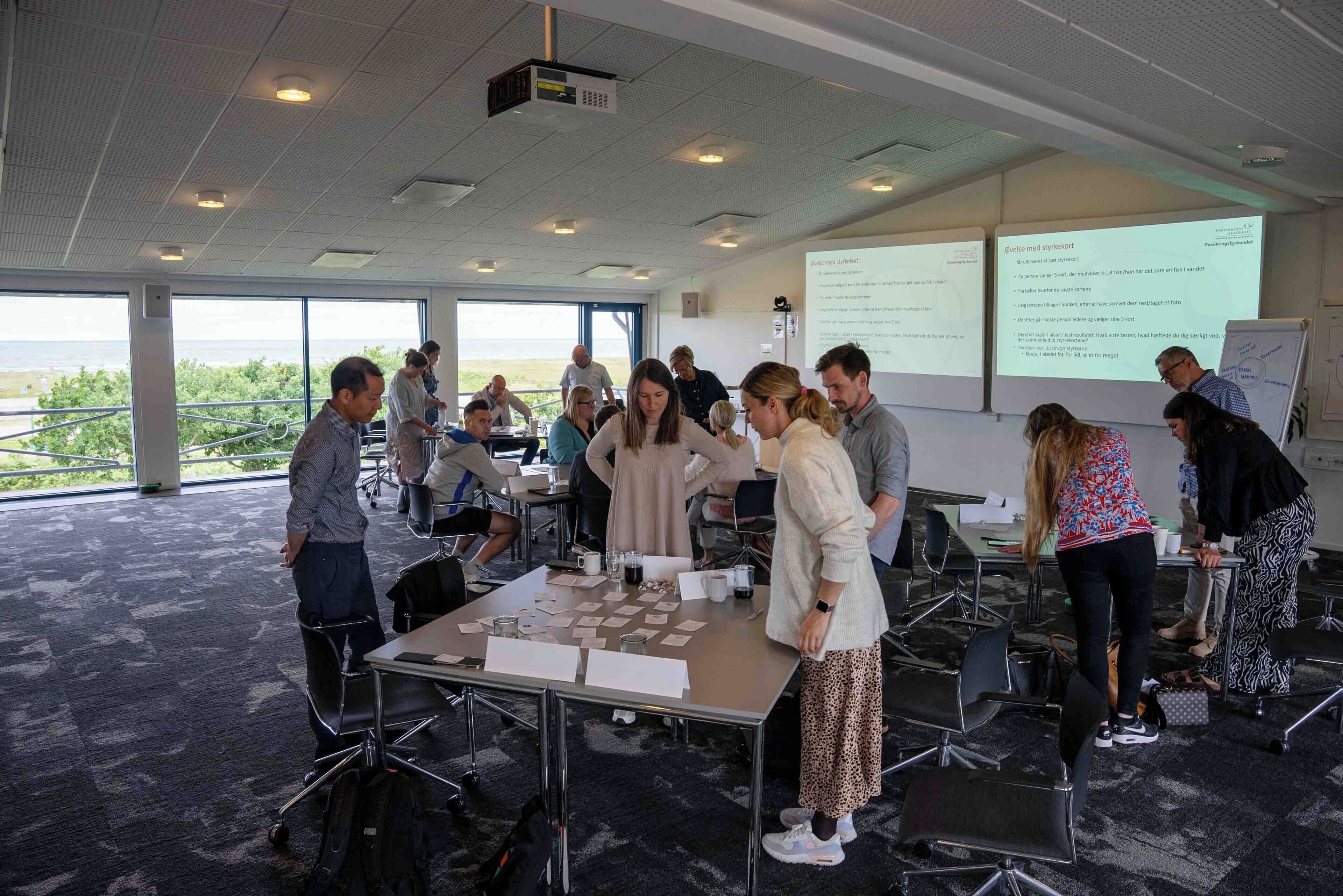 A conference room with a large projection screen, tables with papers, and a view of the outdoors.