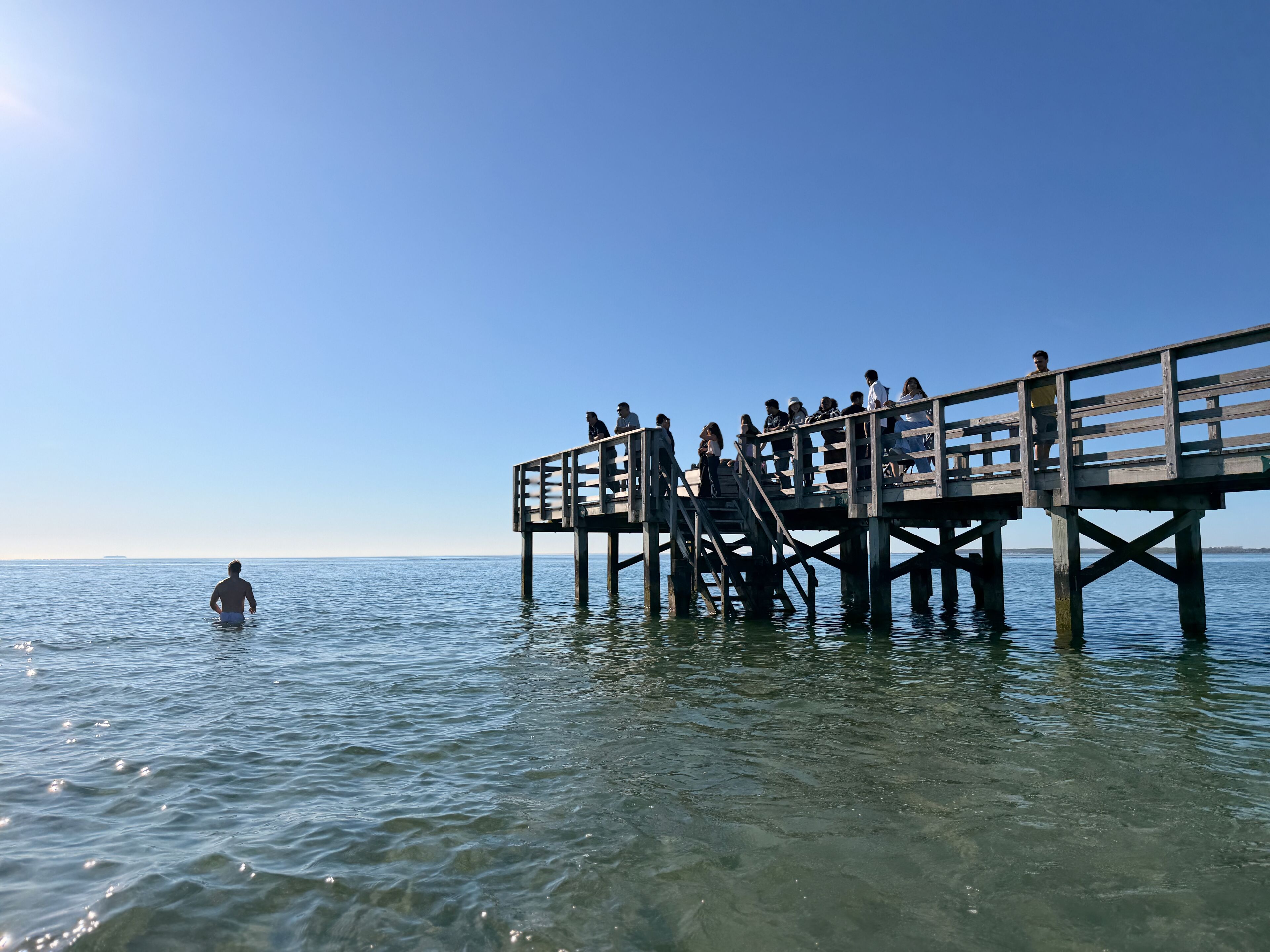 A wooden pier extending into calm water with clear skies above.