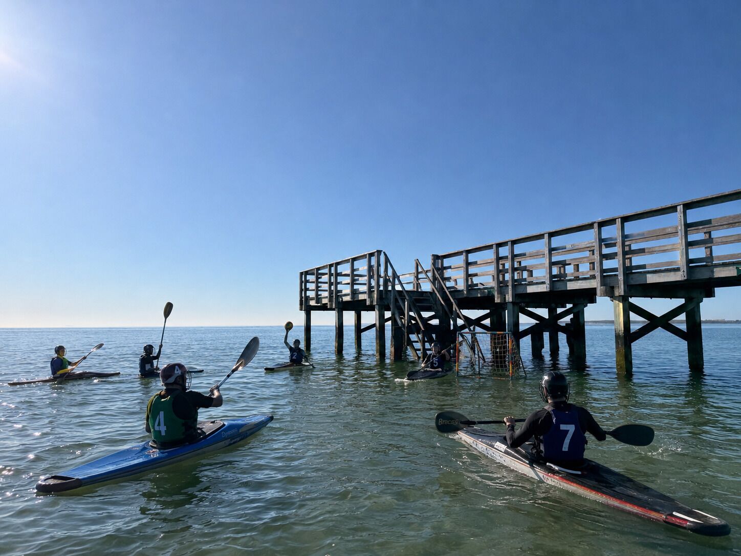 Kayakistes en una calma extensió d'aigua amb un moll de fusta al fons.