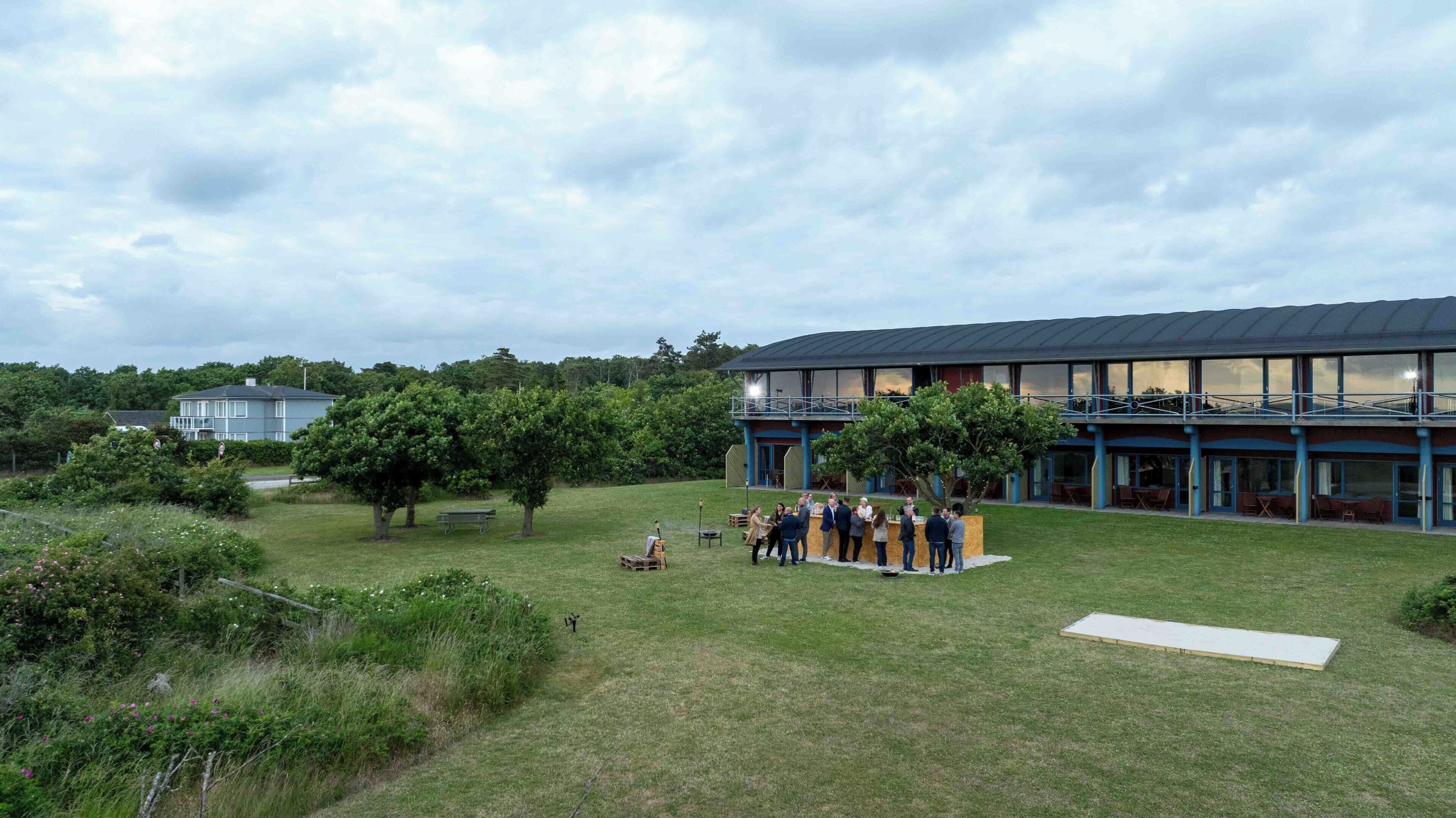 A building with a flat roof, large windows, and a balcony overlooking a grassy area with trees.