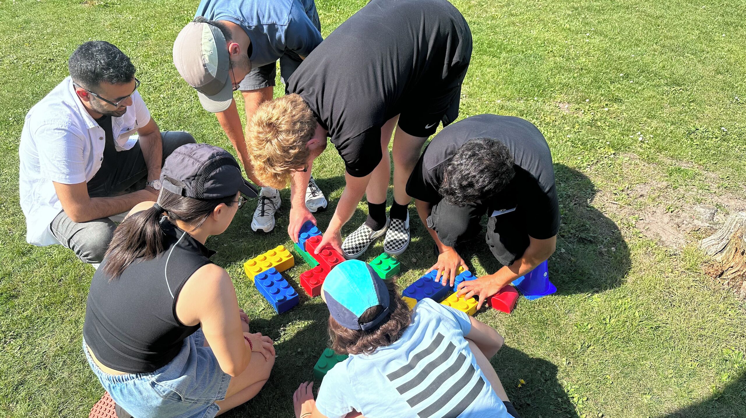 Eine Gruppe von Menschen sitzt auf der Wiese und spielt mit bunten Bauklötzen.