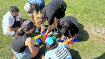 Eine Gruppe von Menschen sitzt auf der Wiese und spielt mit bunten Bauklötzen.