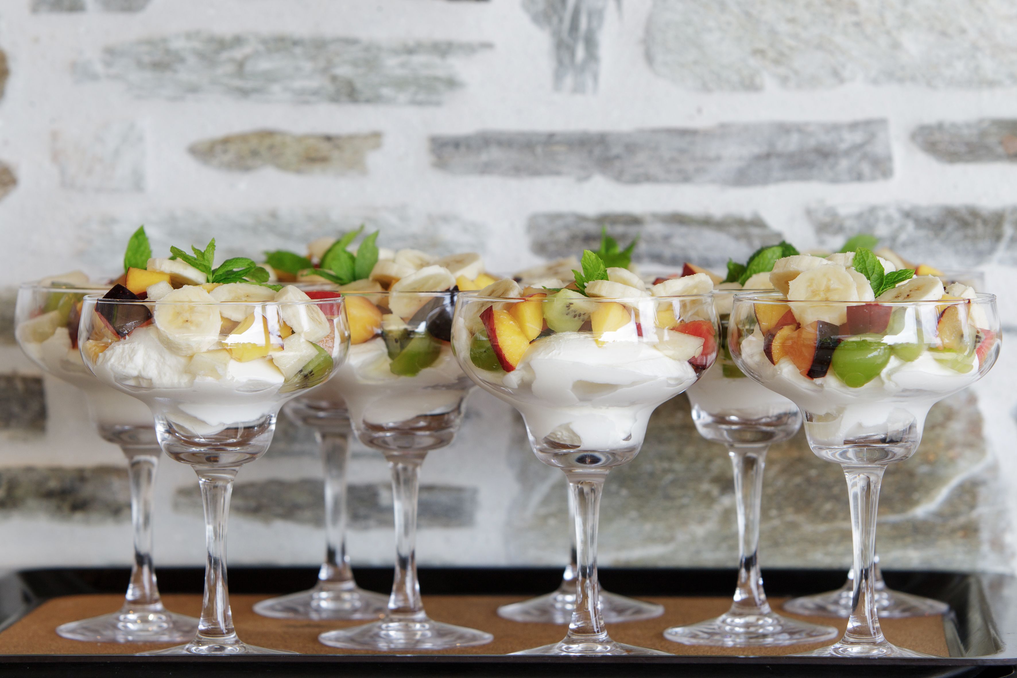 Vier Gläser mit Obstsalat und Schlagsahne, garniert mit Minzblättern, auf einer Tablett.