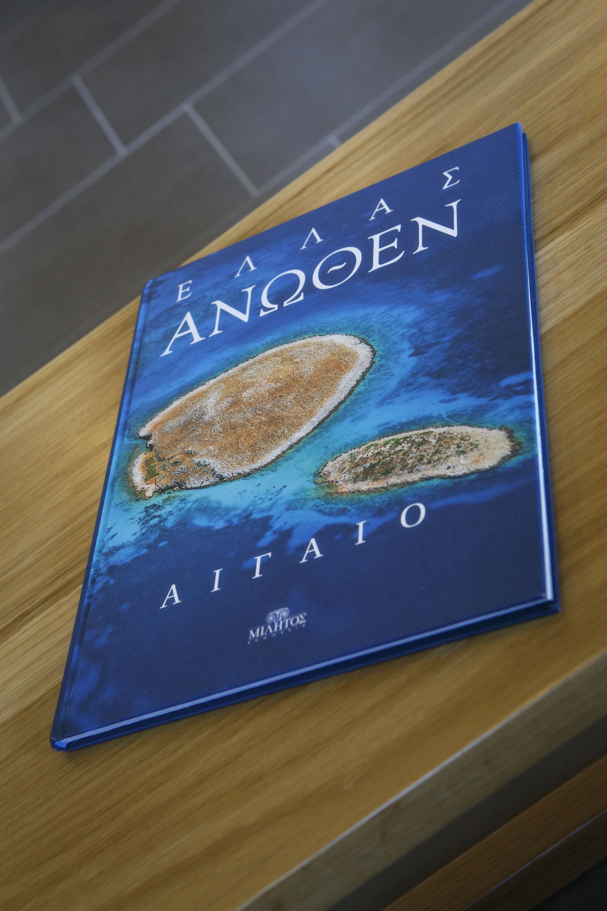 En bok med titeln ”EAAE ANOOEN AITAJO” och en illustration av öar på omslaget.