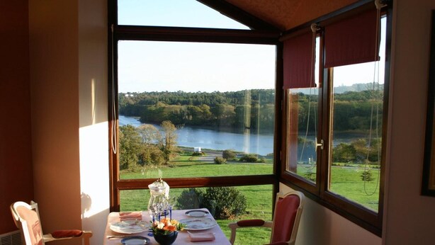 A dining area with a table set for two, overlooking a lake and greenery. - Domaine De Kerstinec (Riec-sur-Belon)