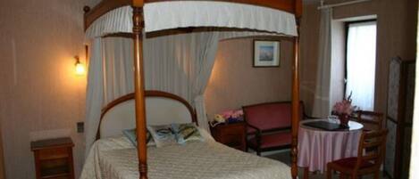 Un lit à baldaquin, une table de chevet, une chaise et une petite table ronde recouverte d’une nappe rose.