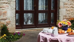 A breakfast setup with a table, a vase of flowers, and a view of a stone building with large wooden doors. - Domaine De Kerstinec (Riec-sur-Belon)