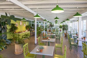Un restaurant avec des chaises et des tables vertes, des plantes en pot et des lampes vertes suspendues.